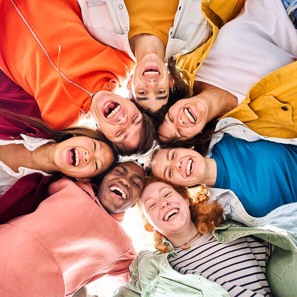 Large multiracial group of smiling young people standing hugging looking at camera. Low angle view.